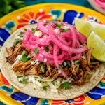 Pickled Red Onions on a taco with lime wedges.